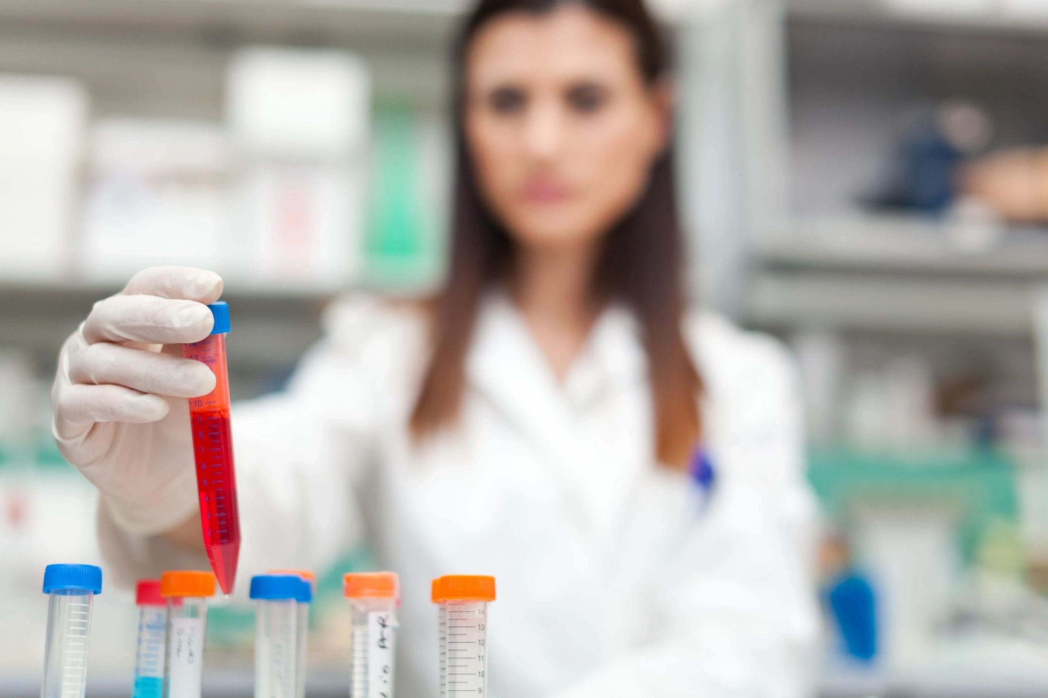 A woman in lab coat holding up a red tube.